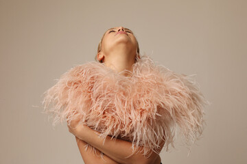 Indoor portrait of beautiful blond young woman wearing pink marabou feathers.