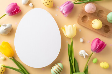 Easter creativity in bloom. Overhead capture of tulips, wooden container with dyed eggs, and small bunny ornaments on a pastel beige background, featuring a vacant egg-shaped slot for text or adverts