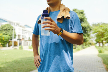 Cropped image of sweaty sportsman drinking water after working out outdoors
