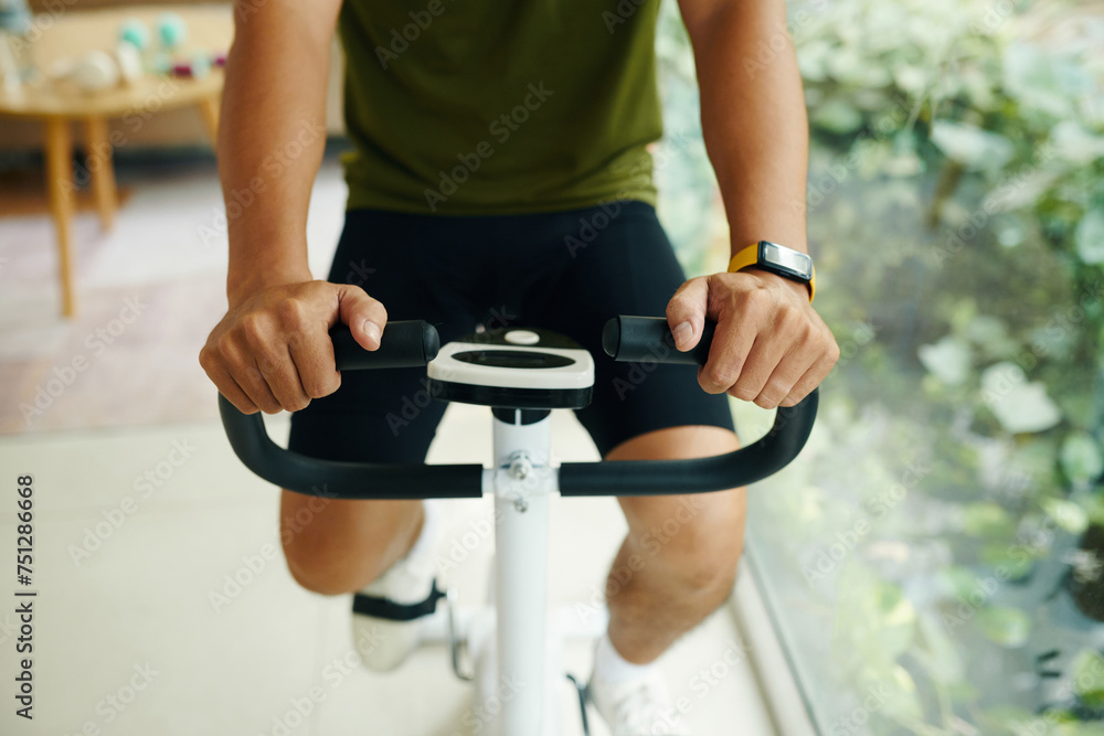 Wall mural Cropped image of man wearing fitness tracker when working out on exercise bike