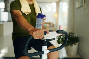 Man drinking water when riding exercise bike at home