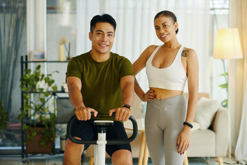 Fit smiling diverse couple exercising on bike at home