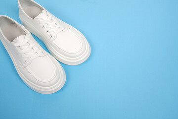 Casual comfortable white shoes.Stylish women's leather shoes with laces on a blue background. Seasonal sales, promotions, discounts on shoes. Proper care for white skin.View from above.Copyspace