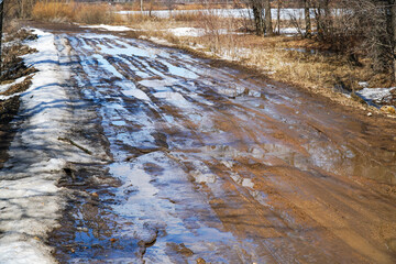 A muddy spring country road with puddles and melting snow
