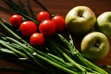 fresh vegetables and fruits closeup on a wooden board. green onions, small cherry tomatoes and apples. preparation for cooking