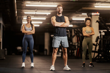 Sportspeople in shape are standing in a gym with arms crossed.