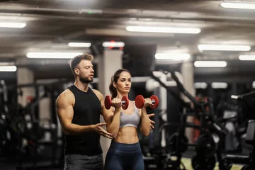  A sportswoman is lifting dumbbells in a gym and personal trainer is helping her. © Dusan Petkovic