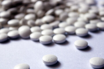 A lot of white pills are scattered on a white background.