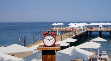 Alarm clock for ten o'clock on beach with jetty and umbrellas. Summer vacation time tourism and...