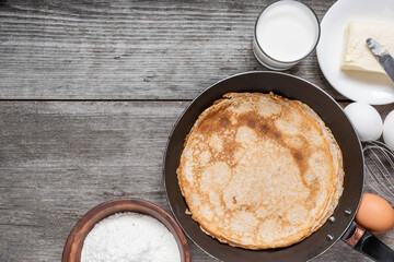 Cooking crepes in frying pan concept. Thin pancakes in a pan with ingredients on rustic wooden table. Top view with copy space. Delicious breakfast