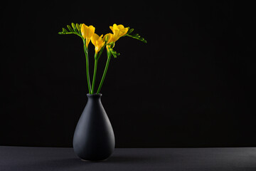 A beautiful bouquet of yellow flower in a stylish porcelain black vase on a black background