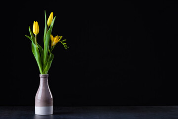 A bouquet of yellow tulips in a vase on the floor.