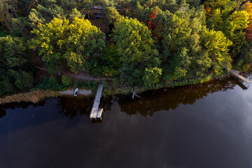 A drone flies over a huge blue lake with a wooden pier among the forests on a cloudless autumn day at dawn. - 751316634