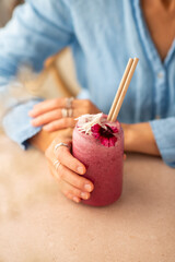 Woman holding a glass of vegan berry smoothie, decorated with edible flower. 