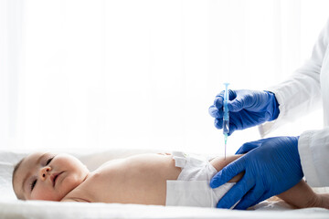 Pediatrician or nurse giving an intramuscular injection of a vaccine to the leg of baby girl. Immunization for children concept.