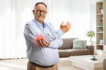 Mature man with pain in elbow standing in a living room