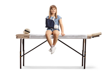 Full length portrait of a girl with a broken arm wearing a sling and sitting on a medical bed
