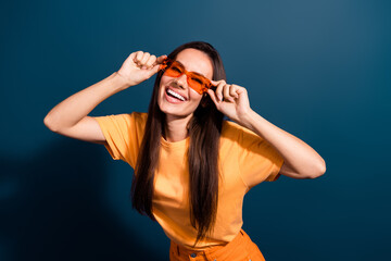 Portrait of good mood adorable woman wear stylish t-shirt hands hold sunglass toothy smiling isolated on dark blue color background