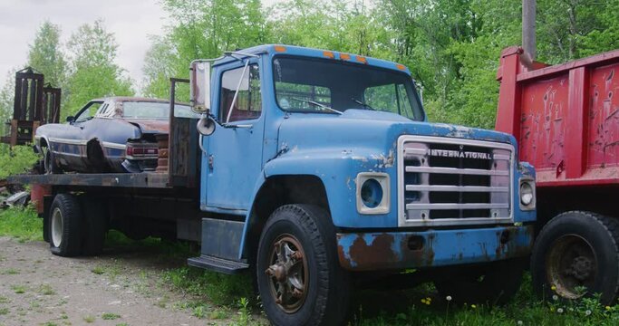A Vintage International Truck rusting away with a Ford Torino from the 1970s sitting on its flatbed surrounded by other scrap cars.