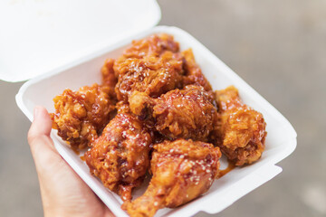 Hand holding deep fried chicken wing with spicy korean sauce in paper box package with street background.