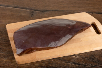 An uncut and unpeeled piece of beef liver on a cutting board.
