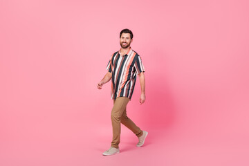 Fototapeta na wymiar Full body length photo of cheerful man in striped shirt and brown pants strolling wear summer outfit isolated on pink color background