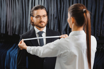 Woman tailor taking measurements of young handsome man, fitting bespoke suit to model. Lux Atelier Classic Menswear