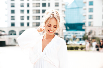 Portrait of young beautiful smiling woman in trendy summer white  dress. Sexy carefree woman posing in the street  at sunset. Positive model outdoors at sunny day. Cheerful and happy