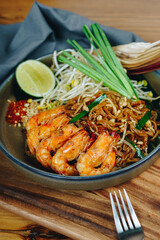 A bowl of shrimp and vegetables with a fork and knife on a wooden table