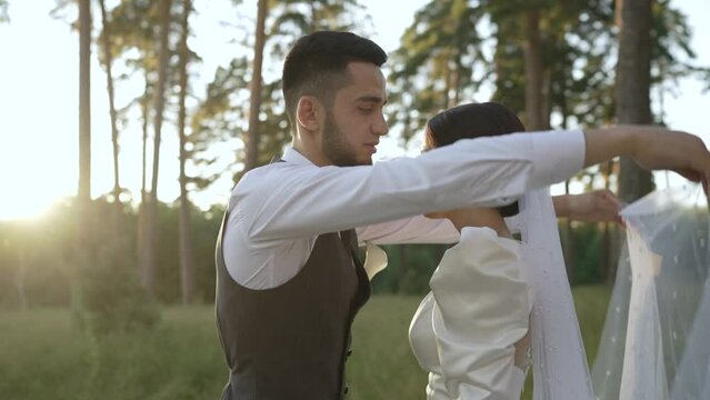 The groom lifts the bride's veil and sees her for the first time. The first meeting of the newlyweds and the first happy hugs. The bride smiles and gently hugs the groom. Wedding ceremony in the fores