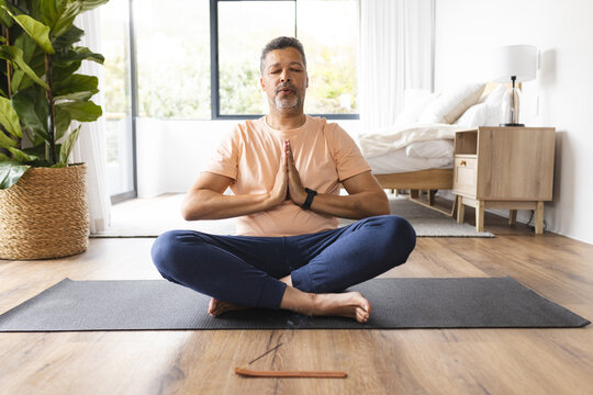 Biracial senior man meditates with hands in prayer position, seated on a yoga mat