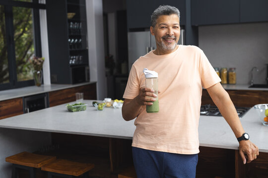 Biracial senior man holding a green smoothie in a modern kitchen - Powered by Adobe
