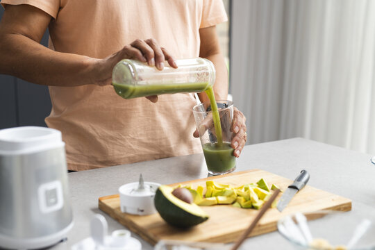 Biracial senior man pours green smoothie into a glass in a modern kitchen - Powered by Adobe