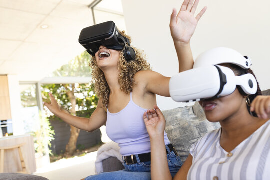 Two young biracial women enjoy a virtual reality experience at home