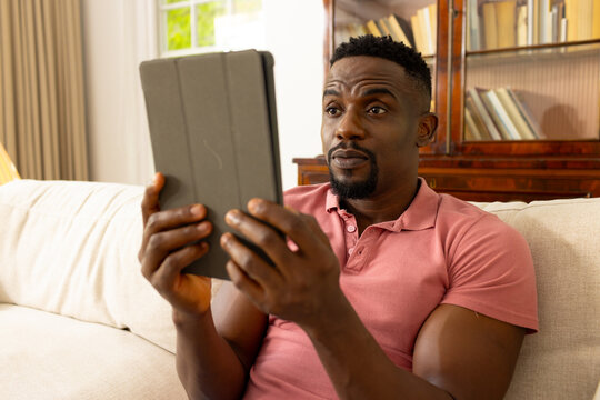 African American man in a pink polo shirt looks surprised at a tablet at home