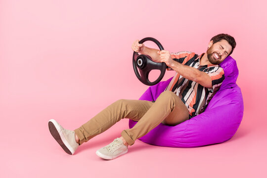 Full length body photo of scared man closed eyes hold steering wheel lying bean bag car accident isolated on pink color background