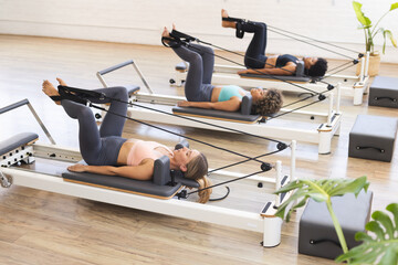 Young Caucasian woman and biracial women exercising on Pilates reformers in a studio