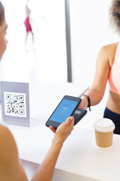 A biracial woman scans a smartphone at a gym reception desk