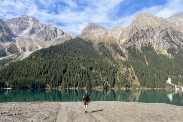 hiker on walking towards an emerald green mountain lake surrounded by high alpine mountains