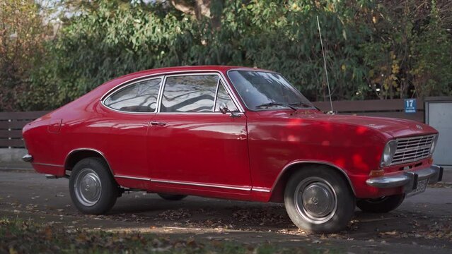 Opel Kadett B Coupe in sixties-seventies red with silver rims in the street in sunny autumn weather. Opel Kadett, Series B, vintage german compact limousine, coupe. Vintage car. 