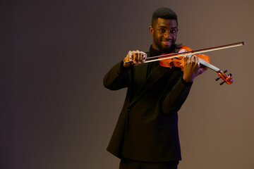 Elegant male musician in black suit playing the violin with passion on a dark background