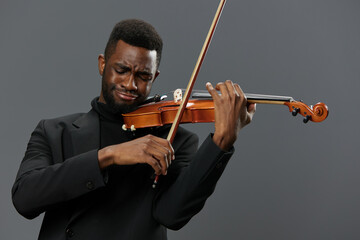 African American man in black suit playing the violin on gray background in elegant musical performance concept