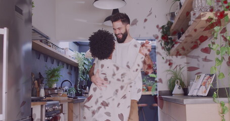 Image of hearts over diverse couple dancing in kitchen
