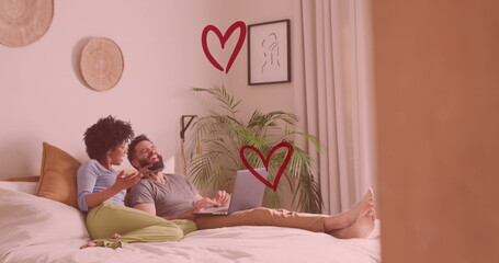 Image of hearts over diverse couple using laptop in bed