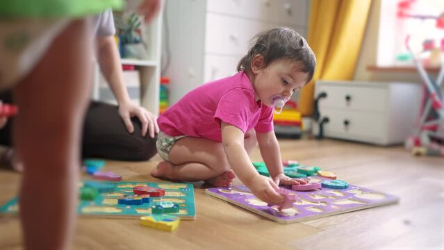 baby daughter plays with toys on the floor develops fine motor skills. Mom plays with her baby daughter, teaches her to put pictures into slots. happy lifestyle family kid dream concept