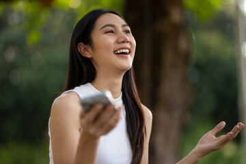 Cheerful young woman uses her smartphone in the park. Expressing happiness and satisfaction