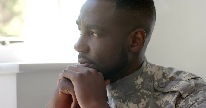 African American soldier in military uniform looks pensive, resting chin on hand at home