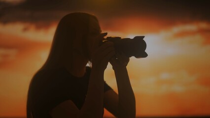 Silhouette of a woman with a camera in her hands at sunset