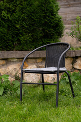 Wicker rattan chair stands in summer garden on background of stone fence. Garden furniture