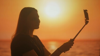 Silhouette of a female, communicating by video call on a smartphone at sunset